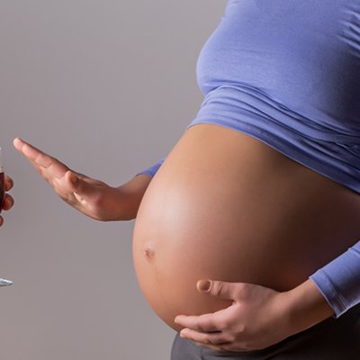 A pregnant woman waves off a glass of red wine.